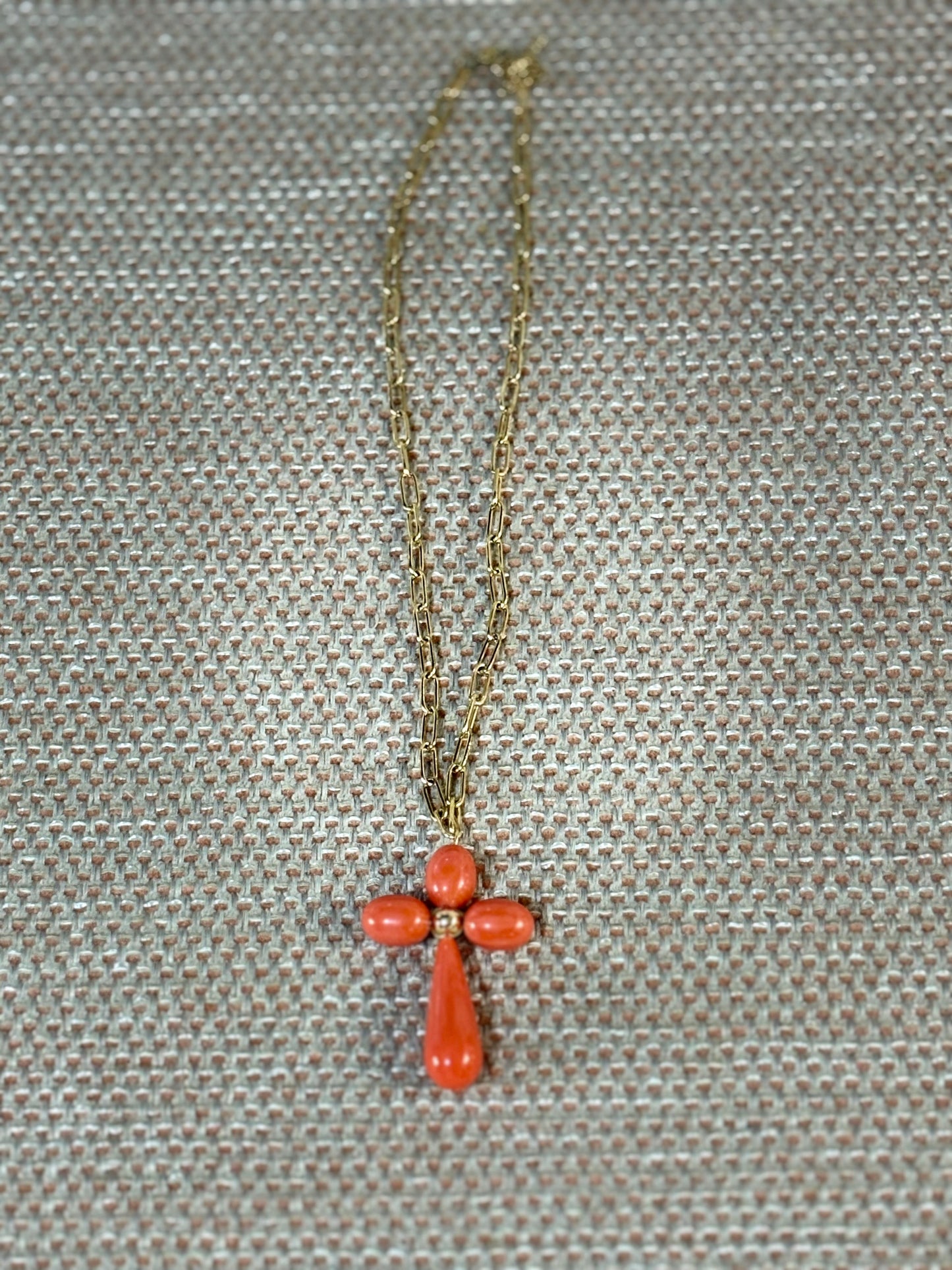 “Collar de cadena dorada con cruz grande de coral anaranjado sobre fondo beige”