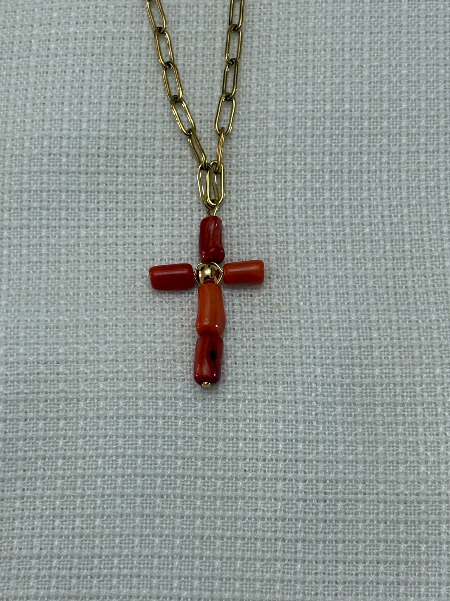“Collar de cadena dorada con cruz de coral oscuro sobre fondo blanco”