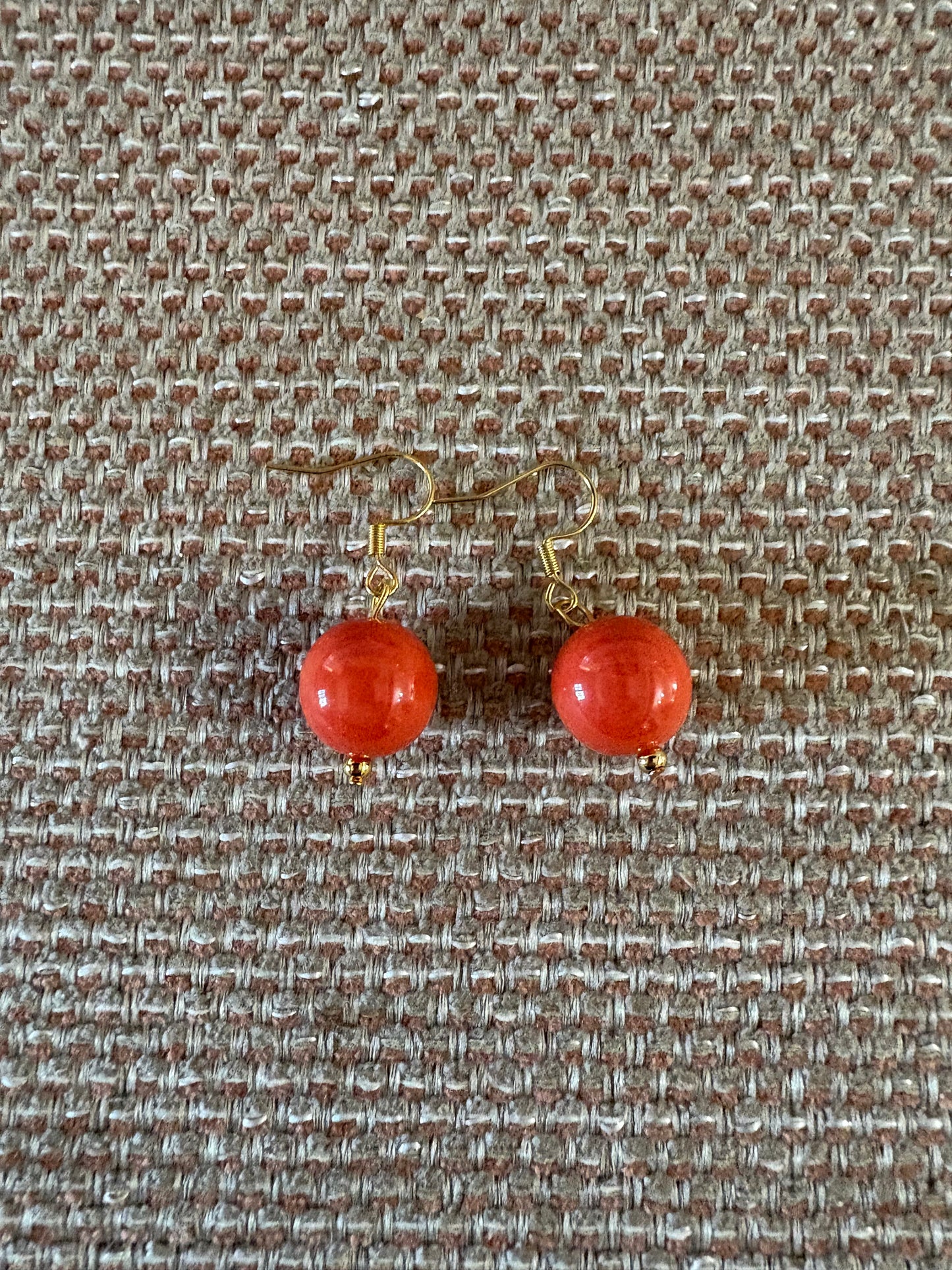 Pendiente de acero con cuenta de coral natural sobre fondo beige