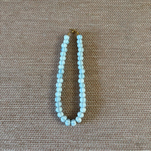 “Collar de bolas caramelo y celeste sobre fondo beige”