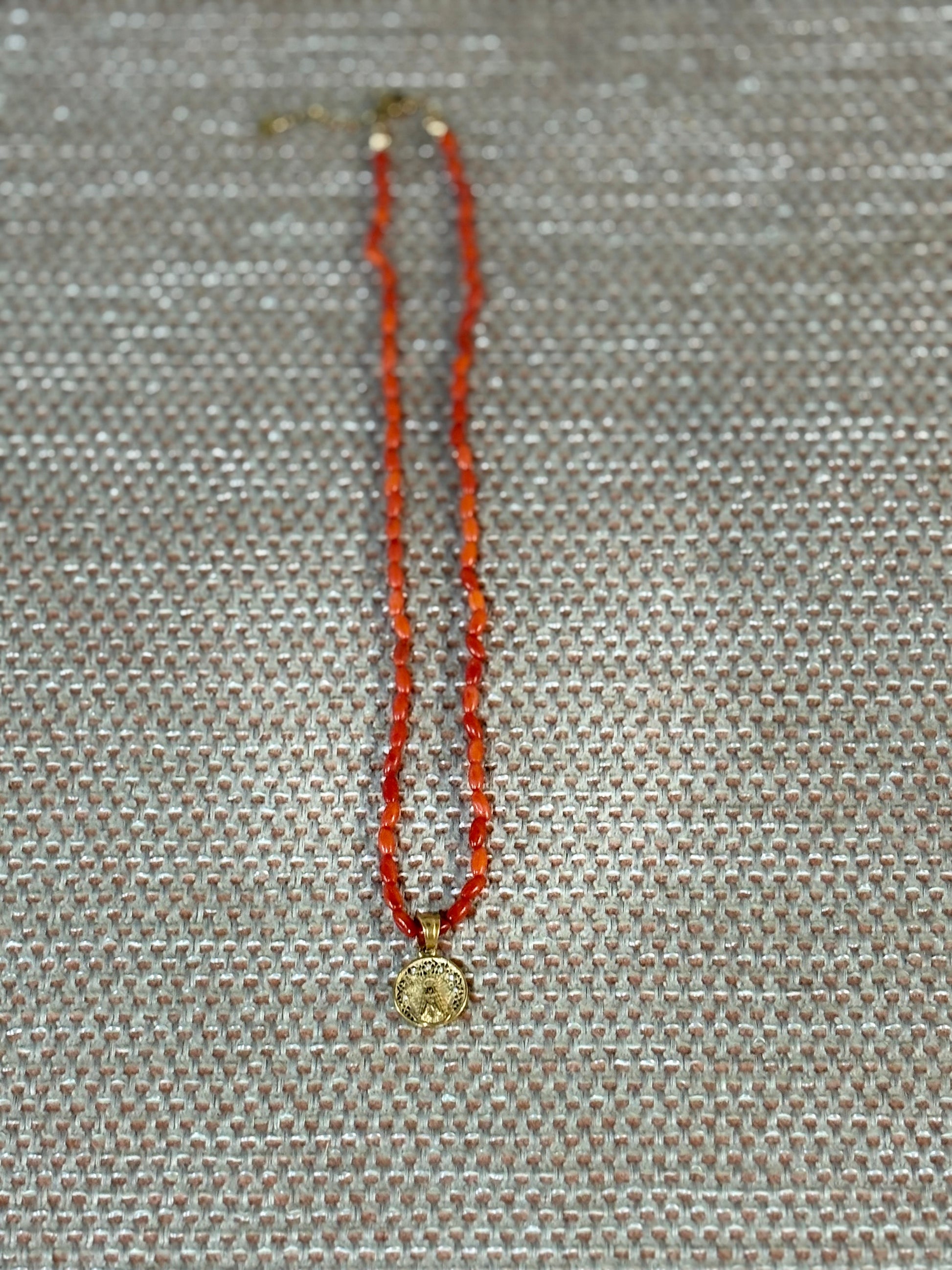 “Gargantilla de coral natural con medalla de la Virgen del Rocío sobre fondo beige”