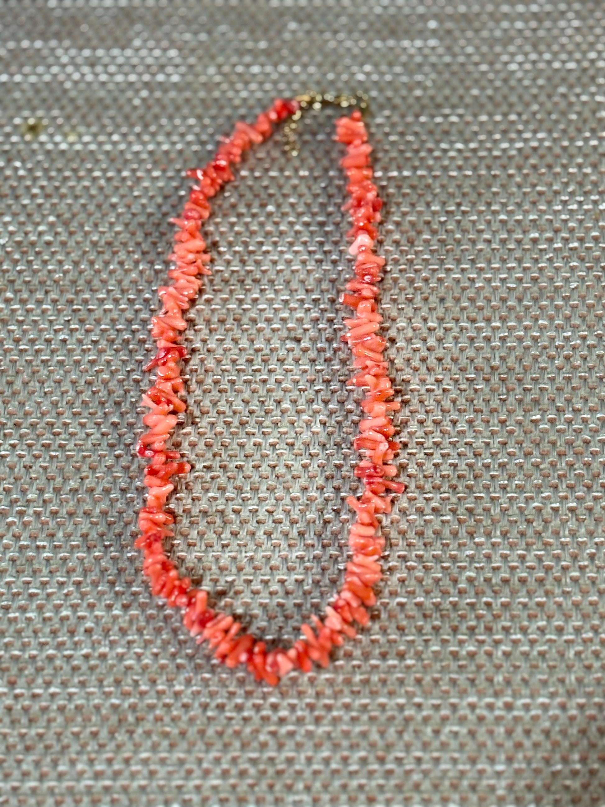 “Gargantilla de coral rosa natural con cuentas irregulares sobre fondo beige”