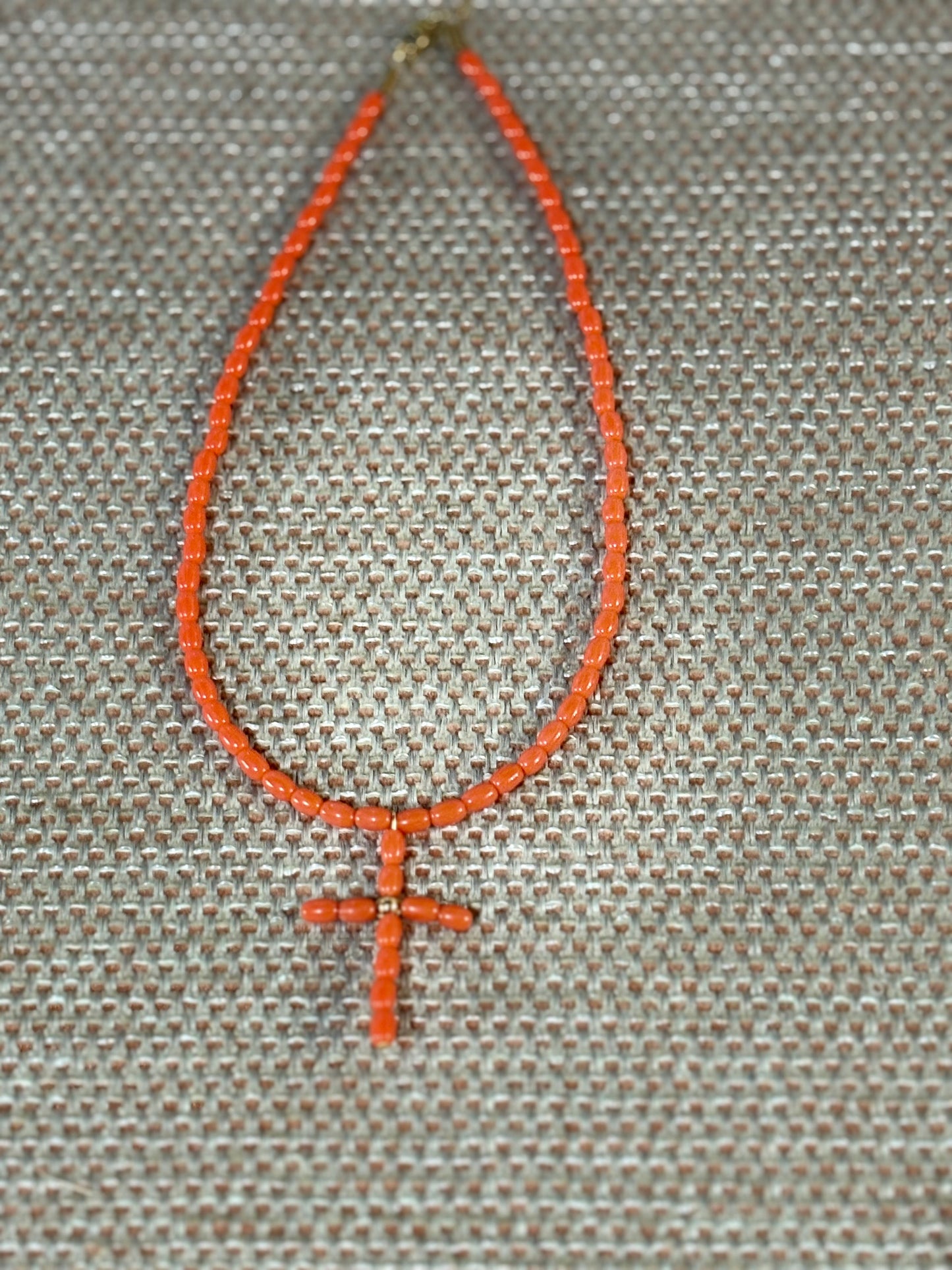 “Gargantilla con cruz en coral rosa natural sobre fondo beige”