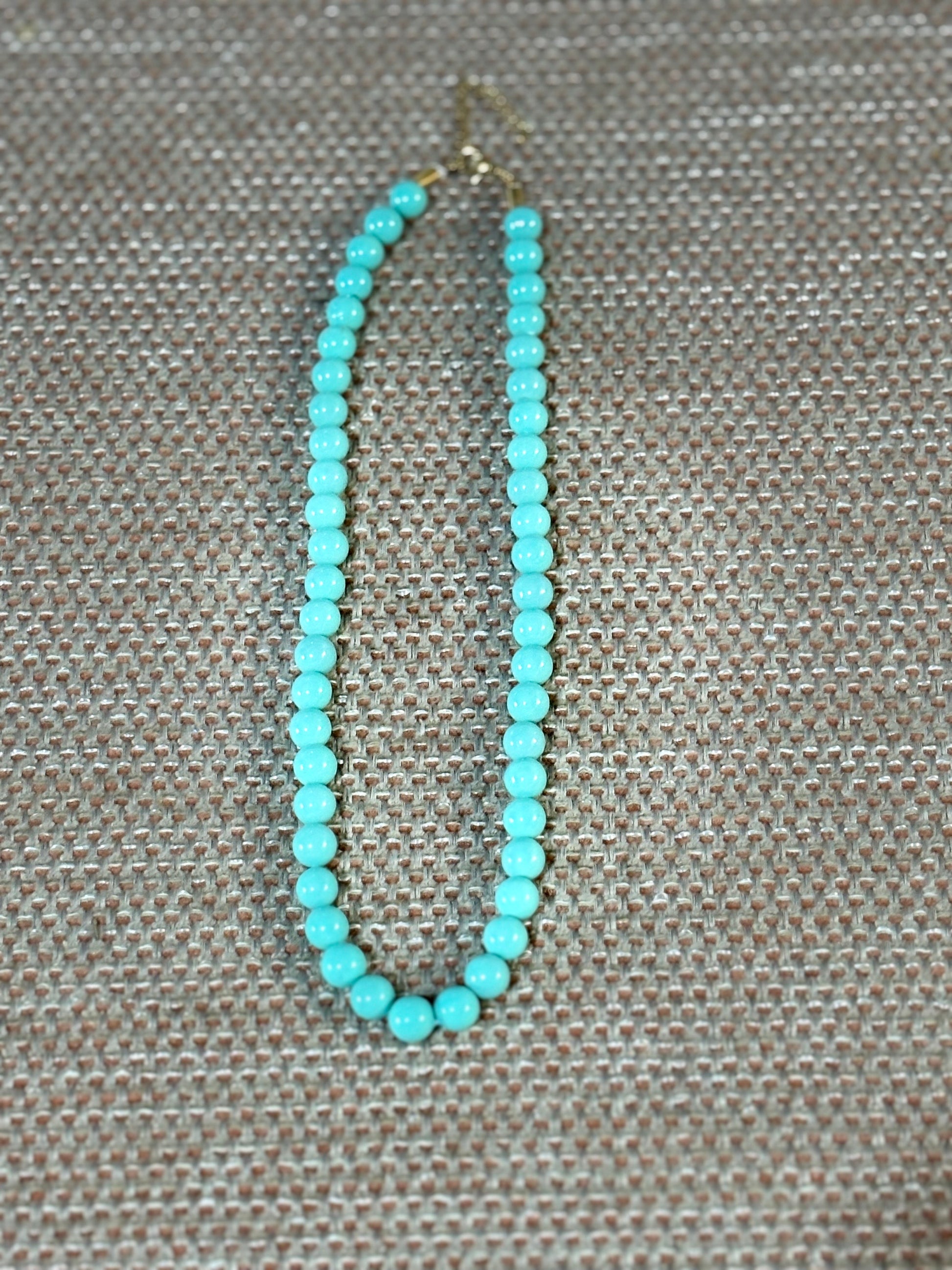 Collar de cuentas redondas de 7 mm color turquesa sobre fondo beige