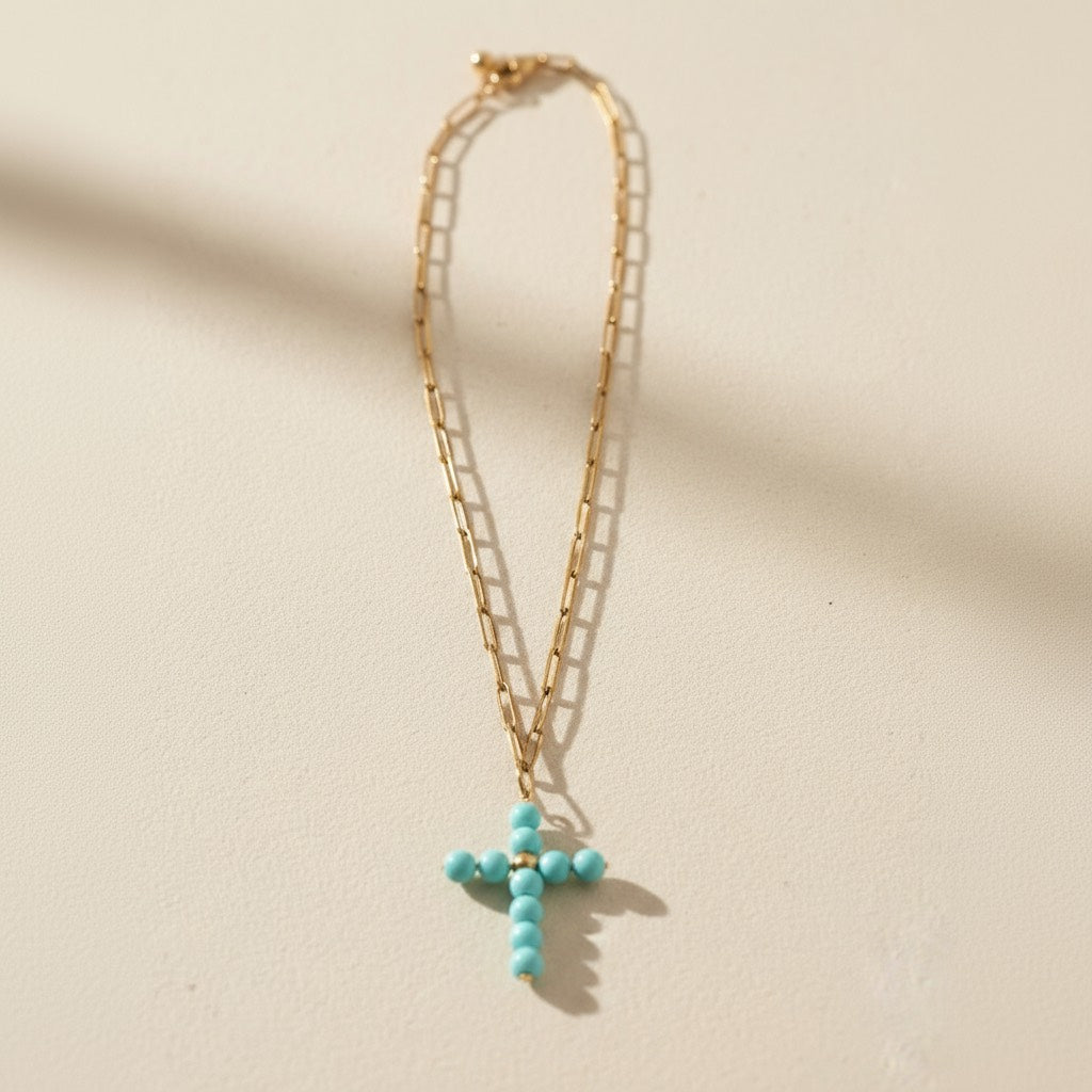 Collar dorado con cruz y cuentas turquesa sobre fondo blanco