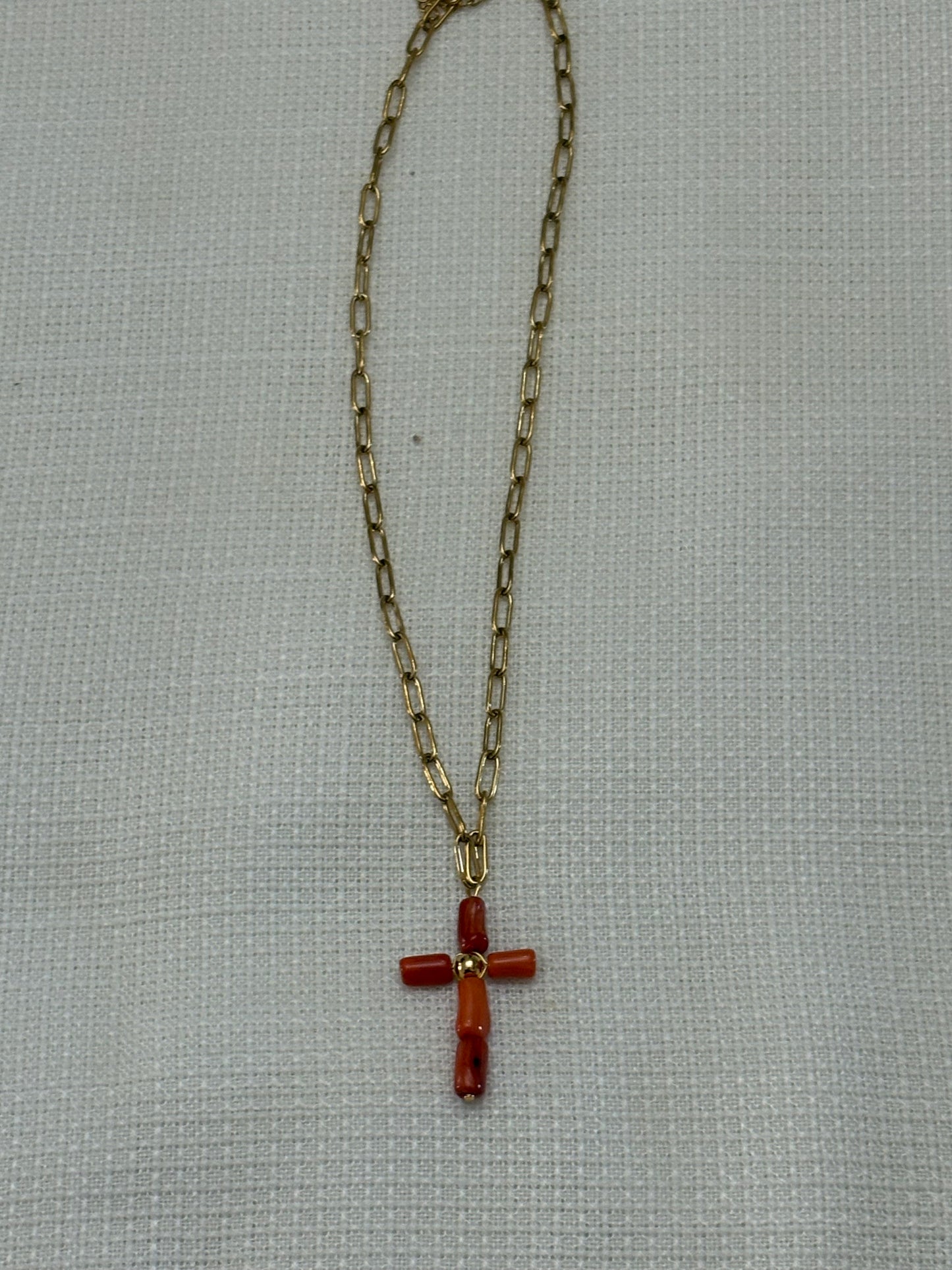 “Collar de cadena dorada con cruz de coral oscuro sobre fondo blanco”