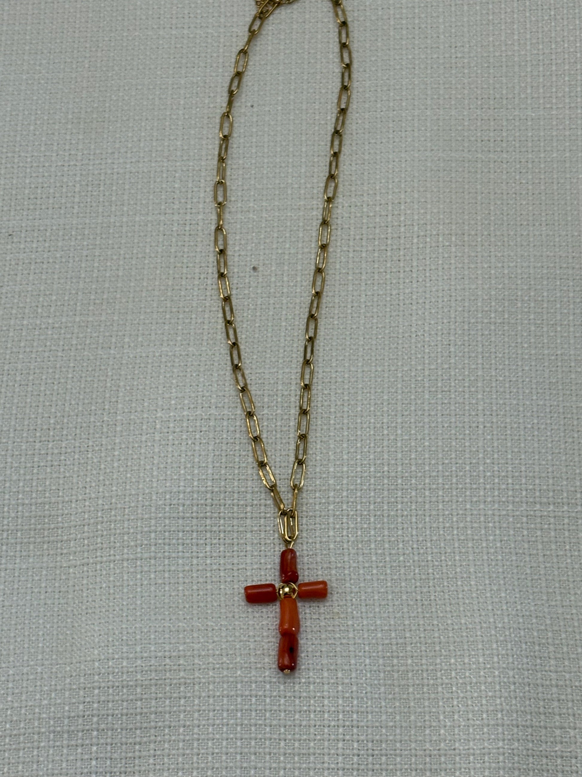 “Collar de cadena dorada con cruz de coral oscuro sobre fondo blanco”