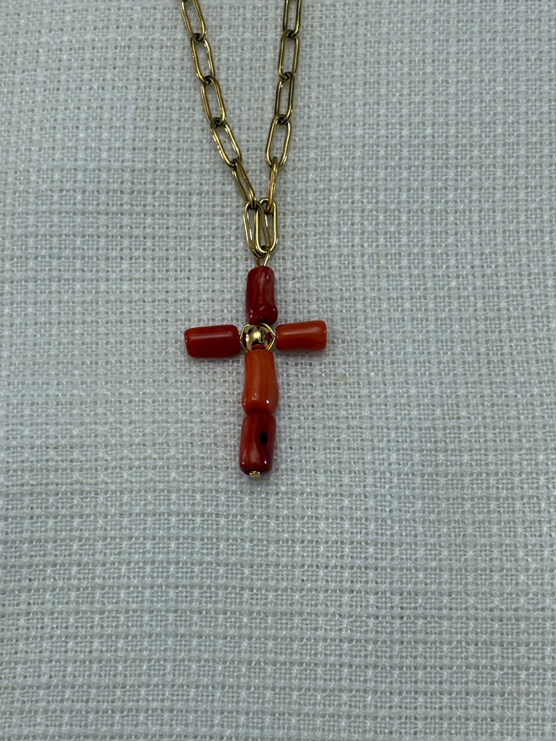 “Collar de cadena dorada con cruz de coral oscuro sobre fondo blanco”