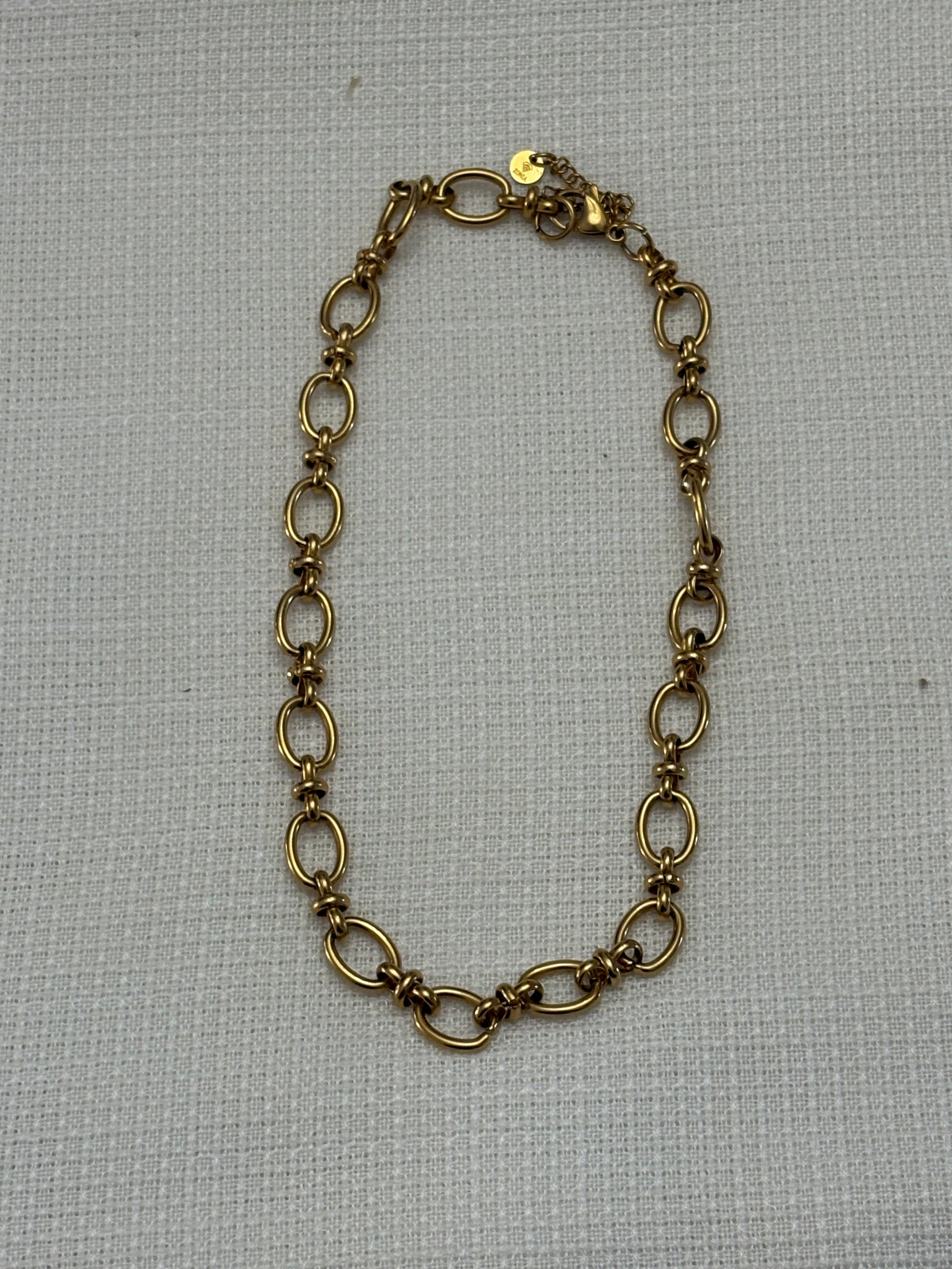 “Gargantilla chapada en oro con pequeños nudos sobre fondo blanco”