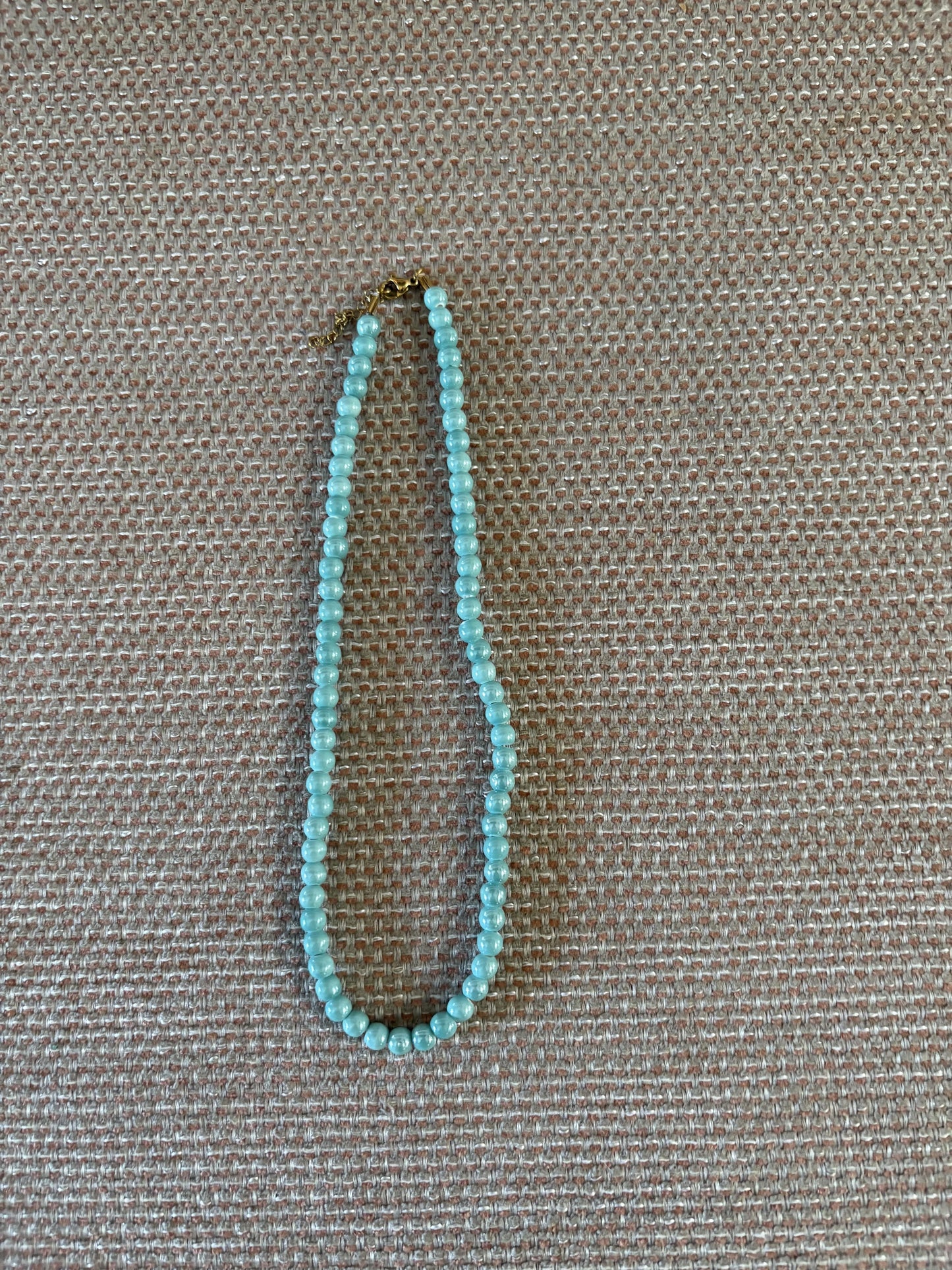 “Collar de bolas turquesa nácarado sobre fondo beige”
