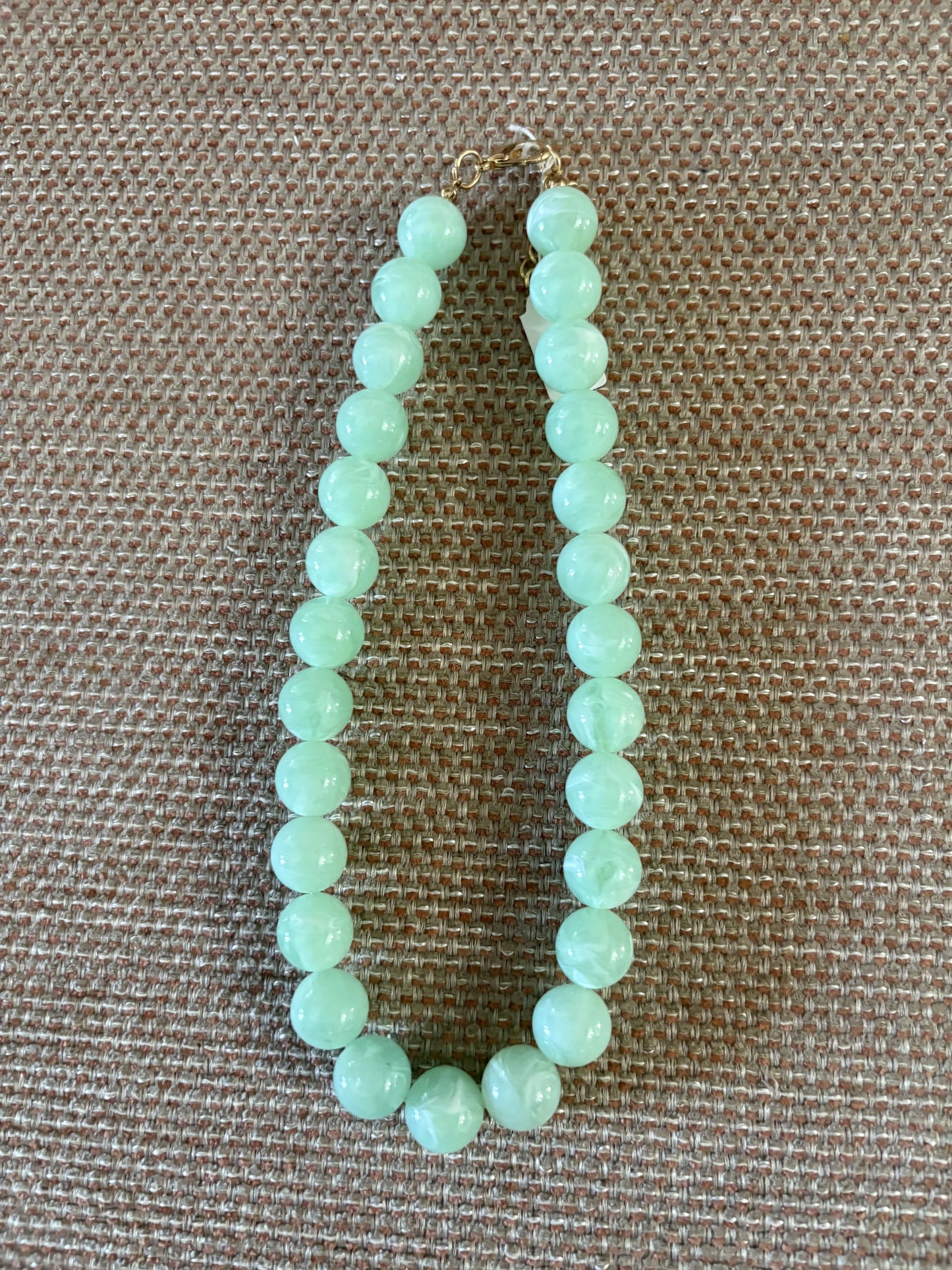 Collar de bolas medianas de resina color verde agua sobre fondo beige