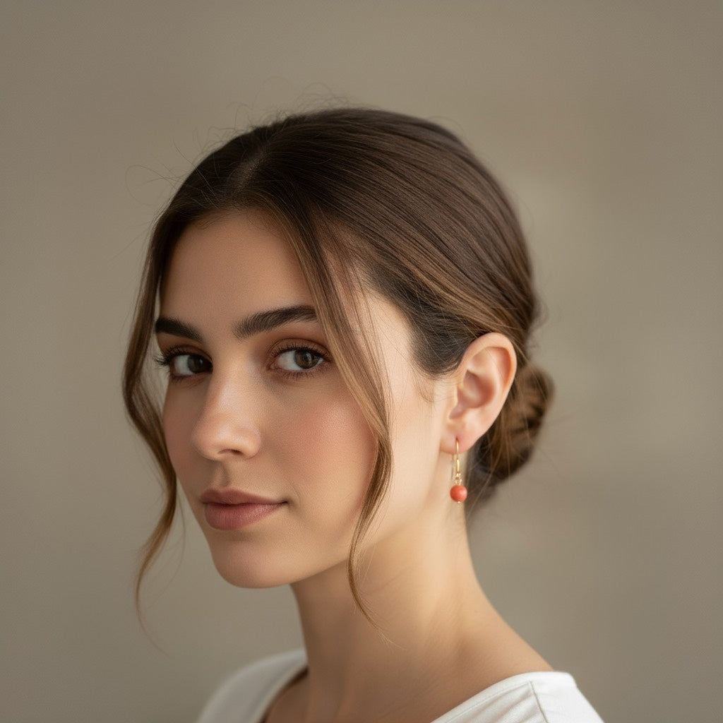 Pendiente de acero con cuenta pequeña de coral sobre fondo blanco