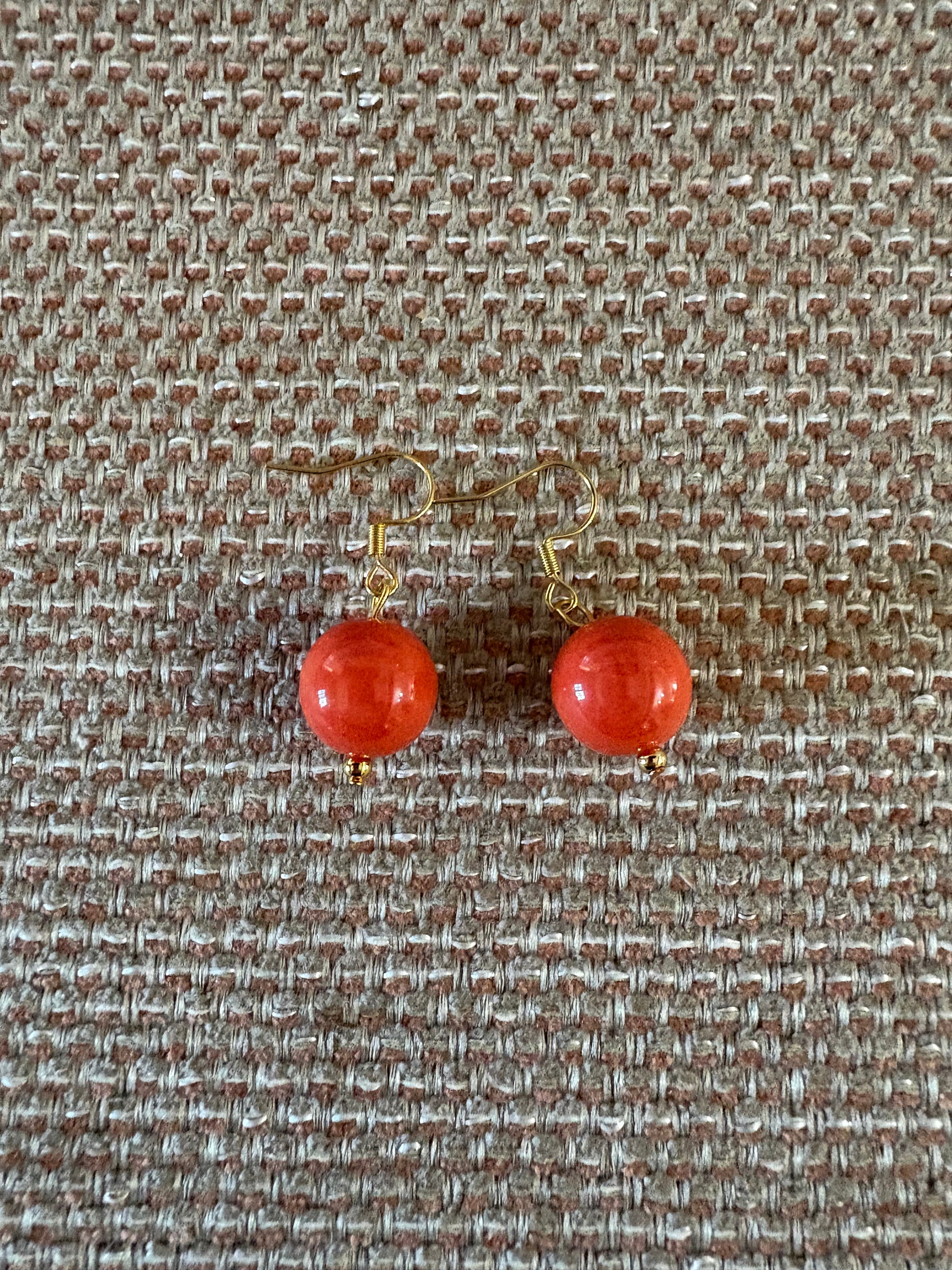 Pendiente de acero con cuenta de coral natural sobre fondo beige