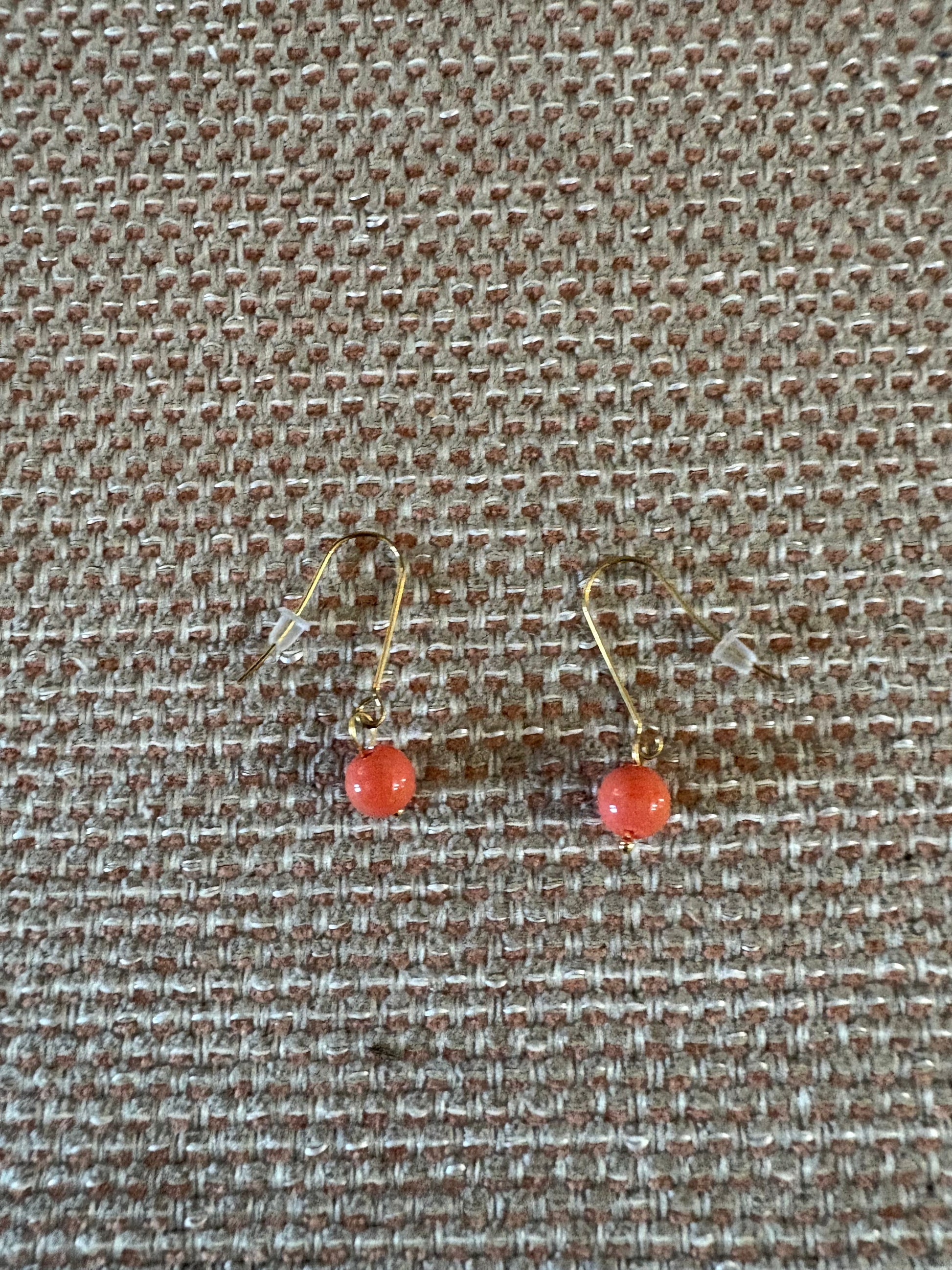 Pendiente de acero con cuenta pequeña de coral sobre fondo beige